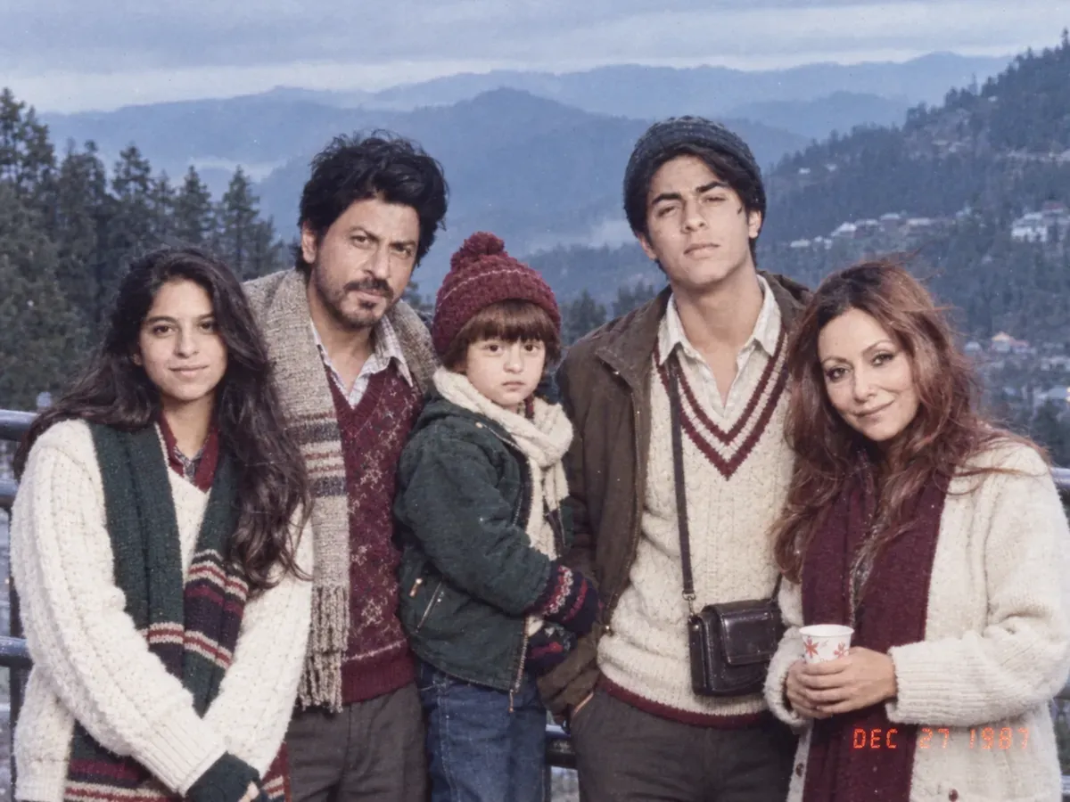 A family in woollen sweaters and caps pressed together at a misty hill-station viewpoint railing in flat overcast 1987 light